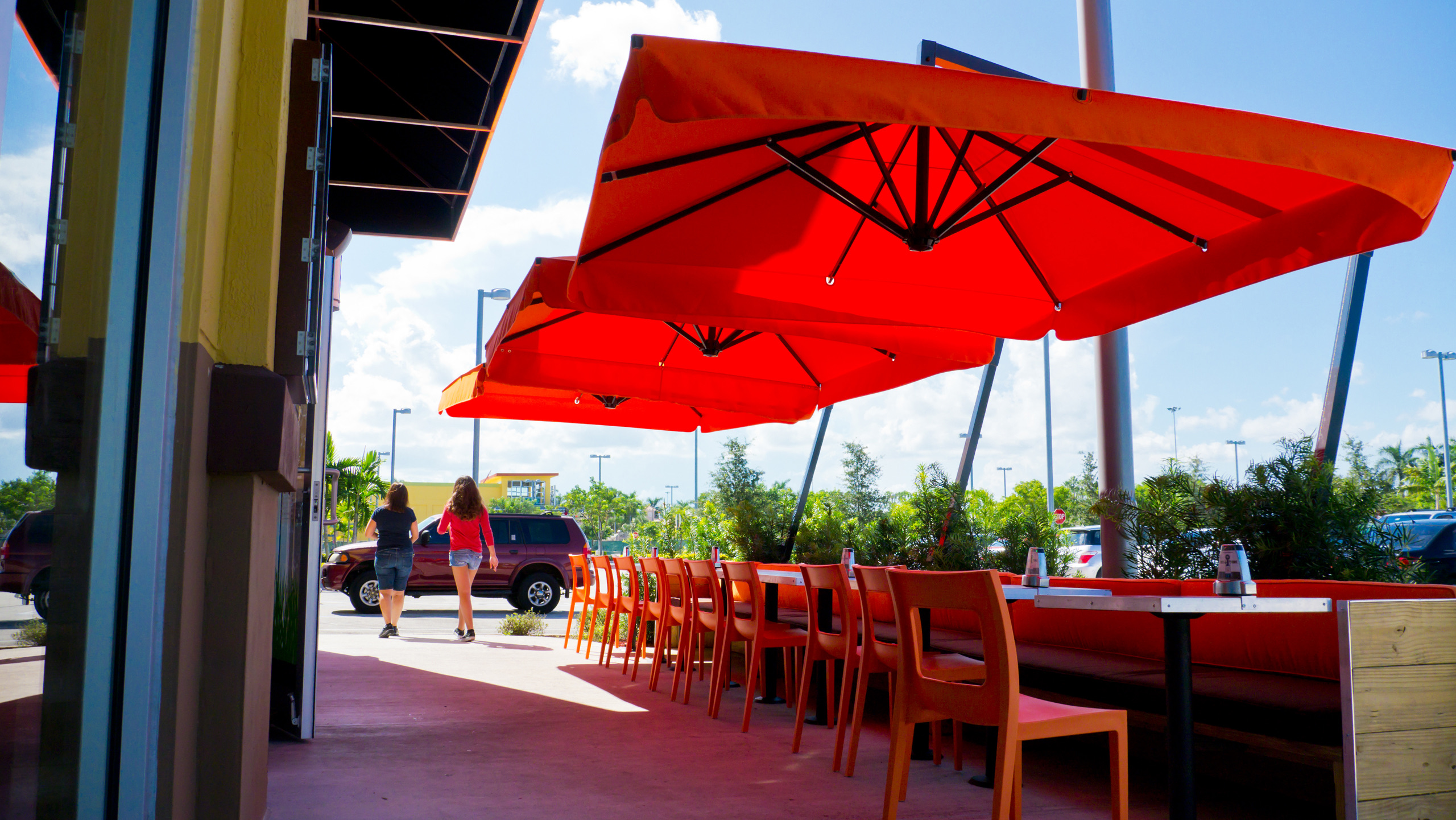 Amalfi cantilever umbrellas with square orange canopies and valances over a long banquette and orange chairs on a restaurant terrace.