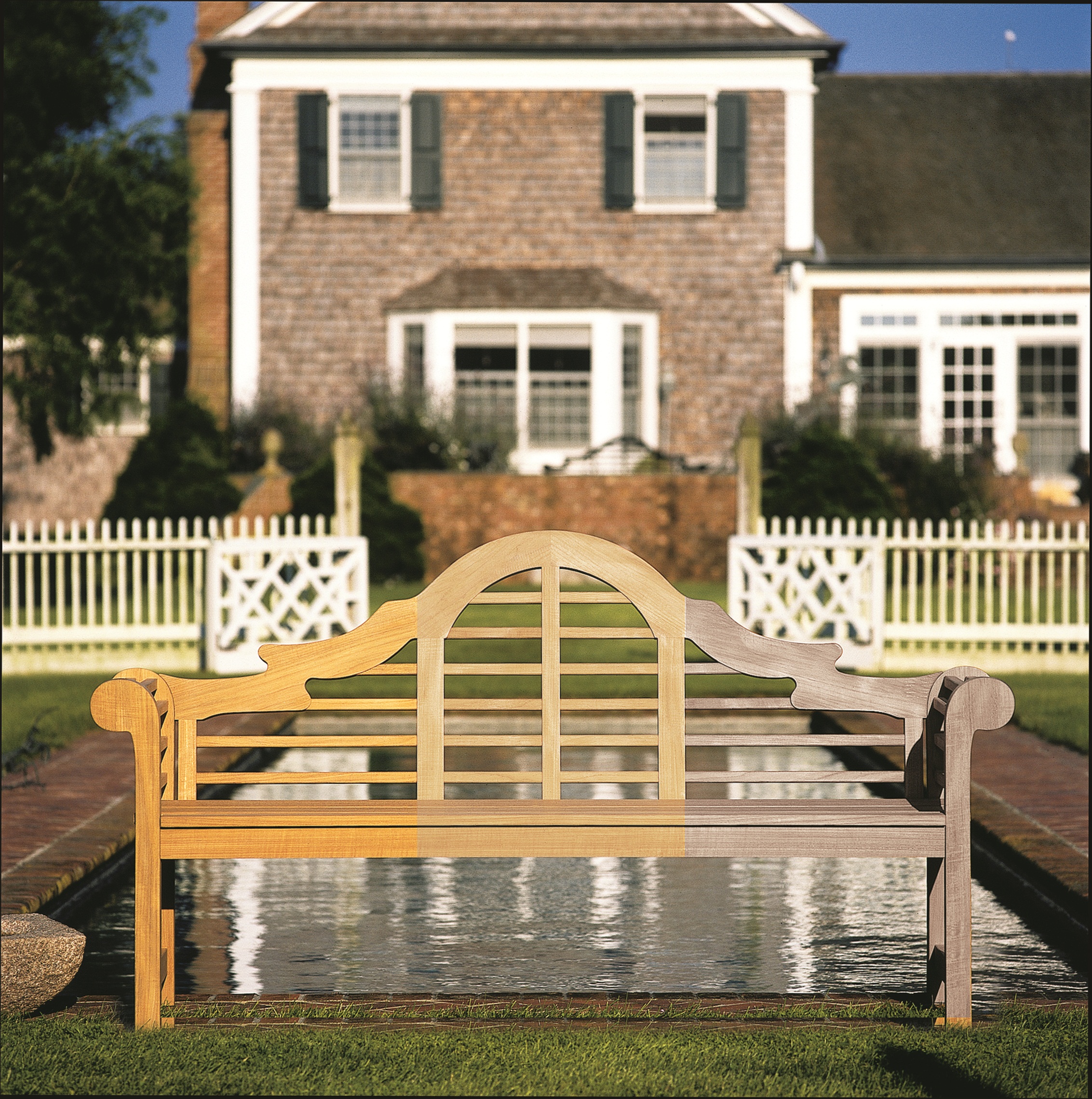 A teak bench outdoors, its timber running from honey through to silver grey across the frame