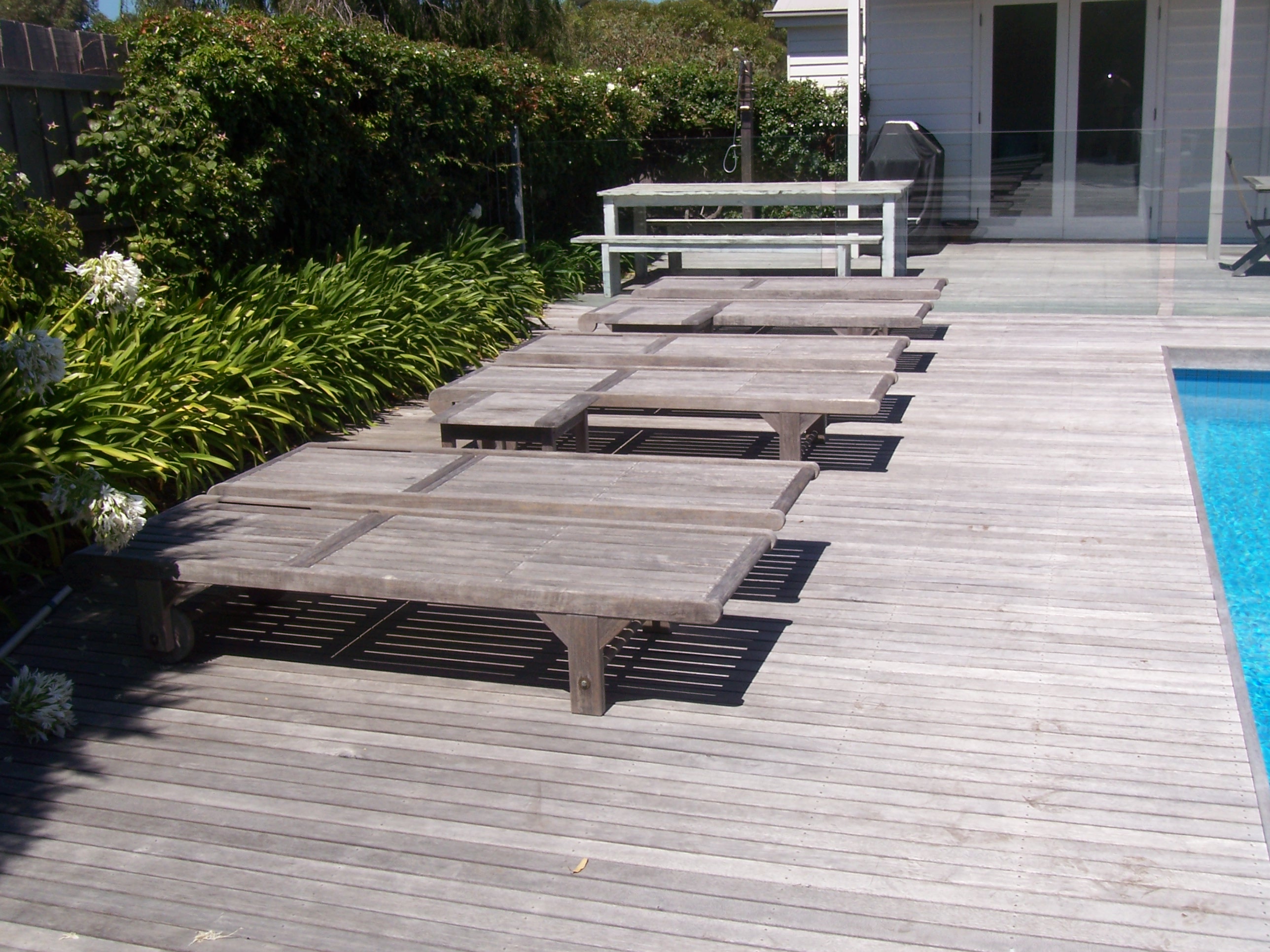 Silvered teak loungers seen from above on a weathered timber deck beside a pool
