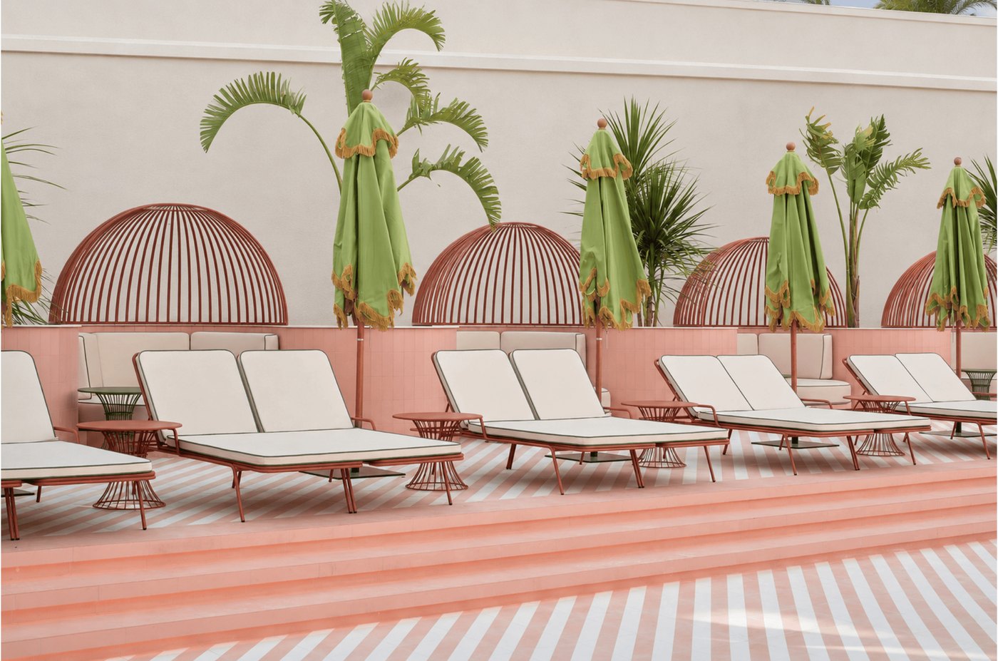 A run of terracotta sunloungers along a pink wall set with arched terracotta screens and palms.