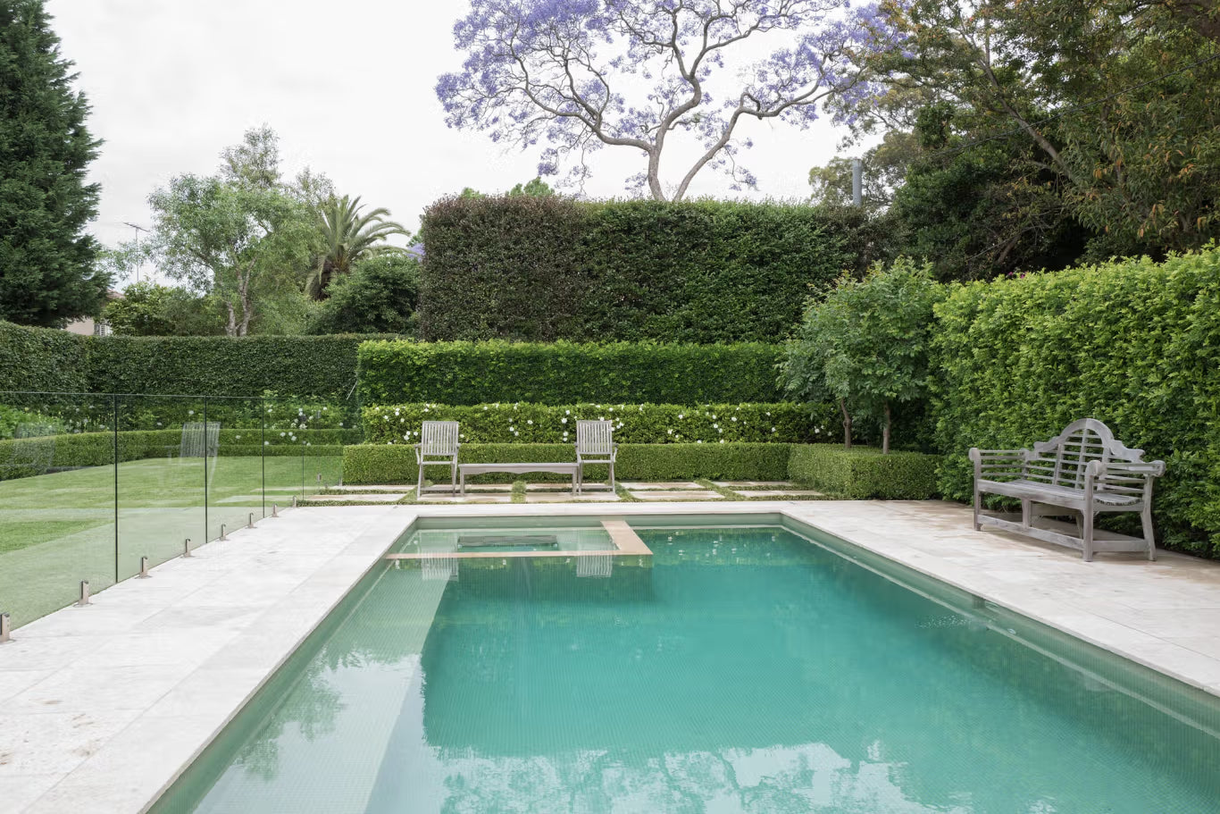Lutyens — A silvered Lutyens bench and two chairs set against clipped hedging at the end of a walled lap pool.