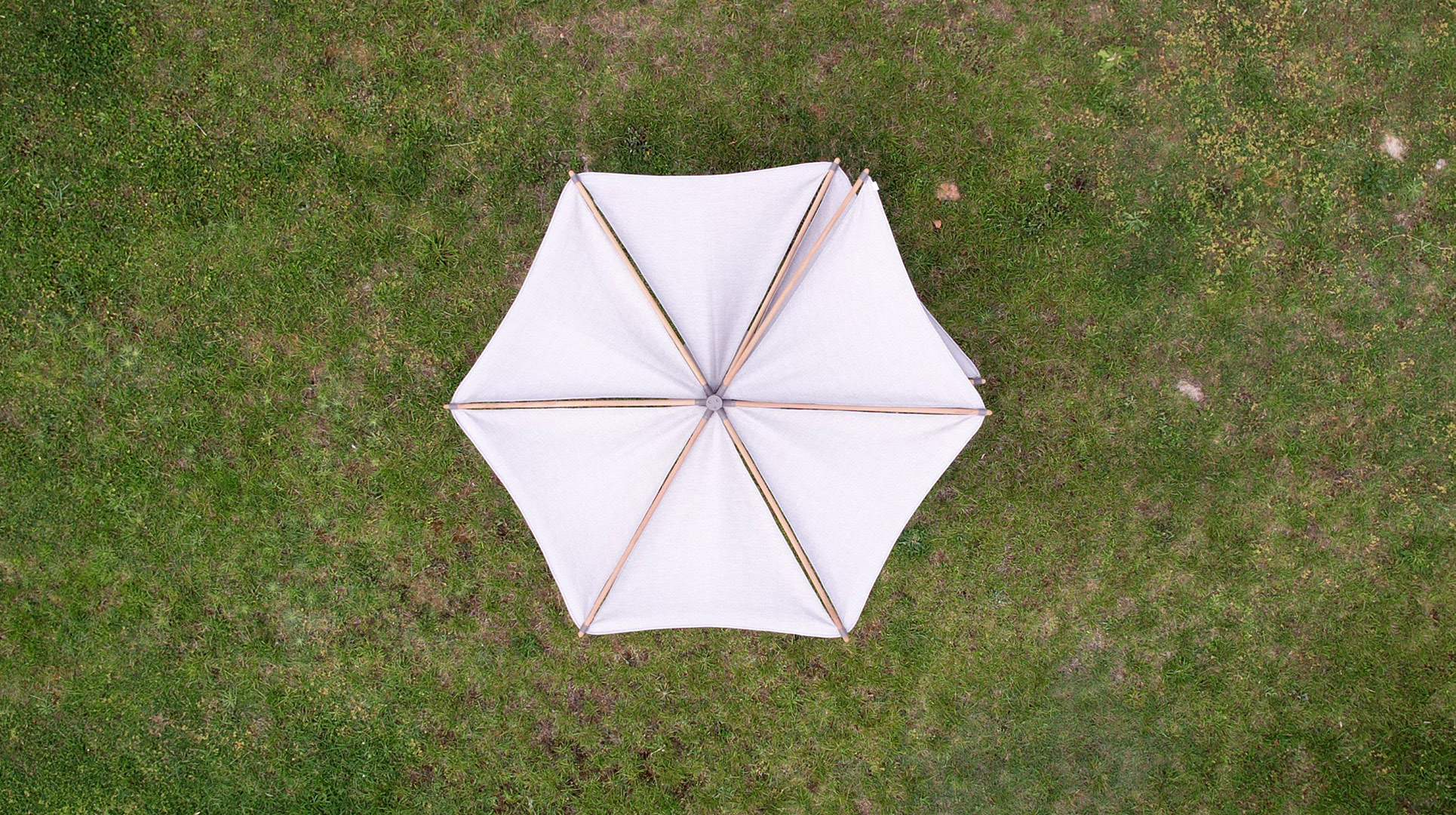 The Om Wood parasol seen from directly above, its canvas canopy open over a matching wood-and-canvas deck chair pair.