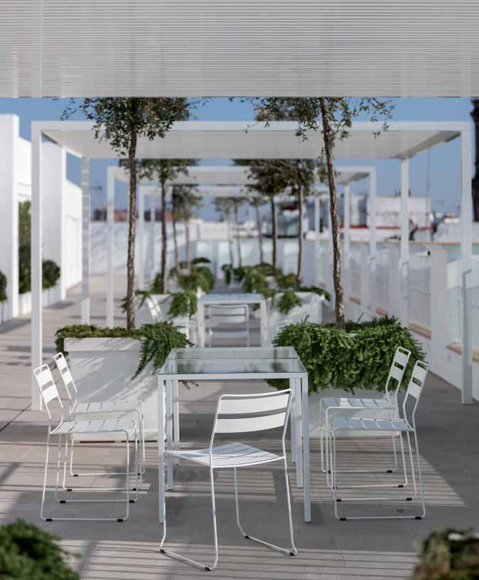 White wire dining chairs and a glass-topped table under a pergola on a rooftop terrace — iSiMAR catalogue photography