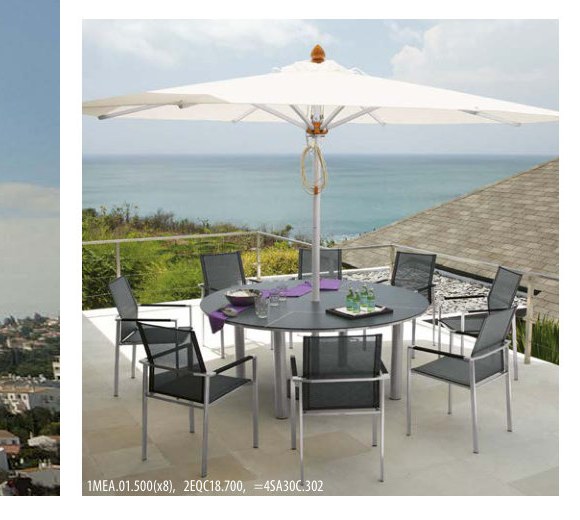 round parasol shading a long dining table set on a terrace overlooking the coast