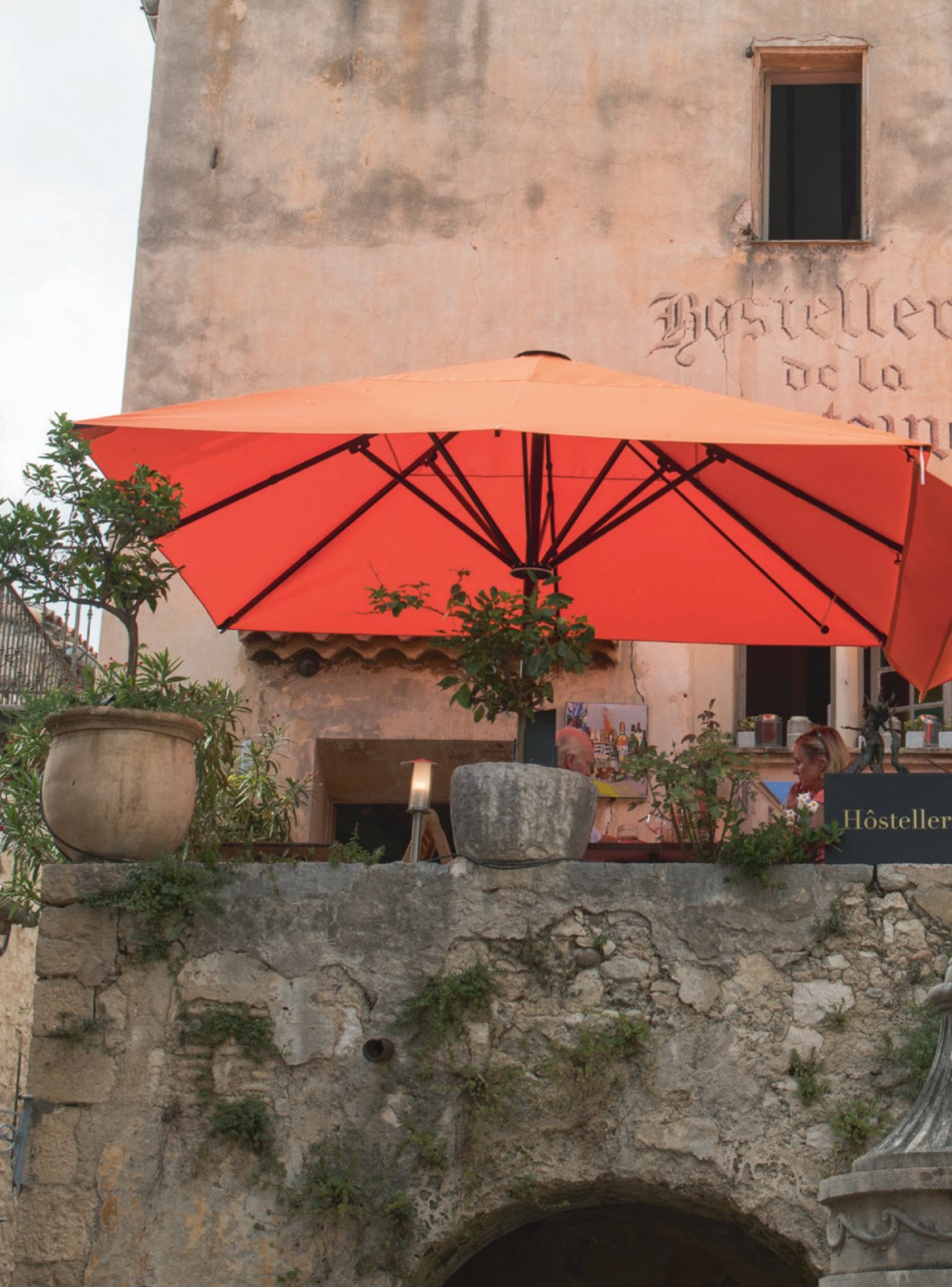 Vivid orange square parasol shading a stone terrace against a weathered building facade