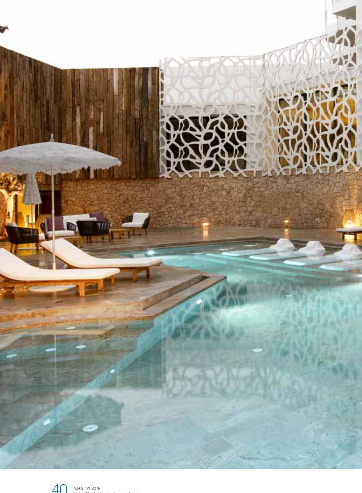 White lace-pattern parasol beside a luxury pool with fretwork screen walls at dusk
