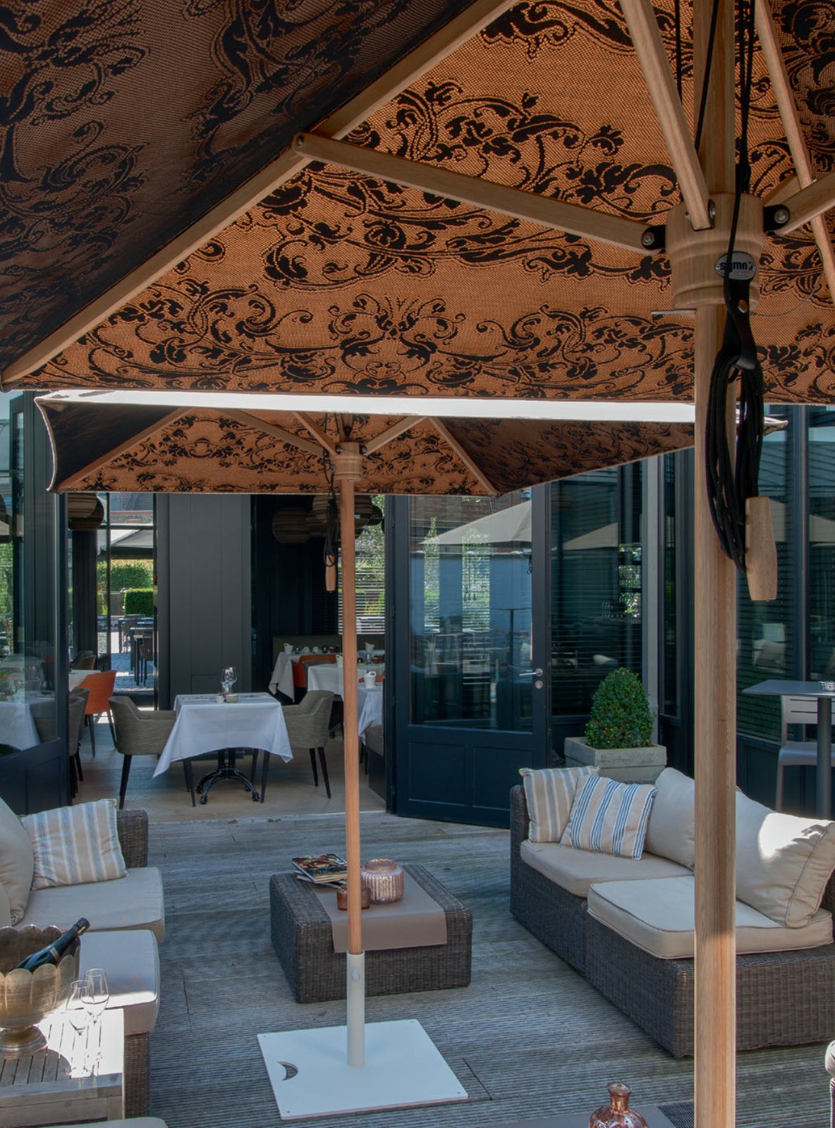 Damask-patterned parasol canopy in gold and black, shading an elegant hotel terrace lounge