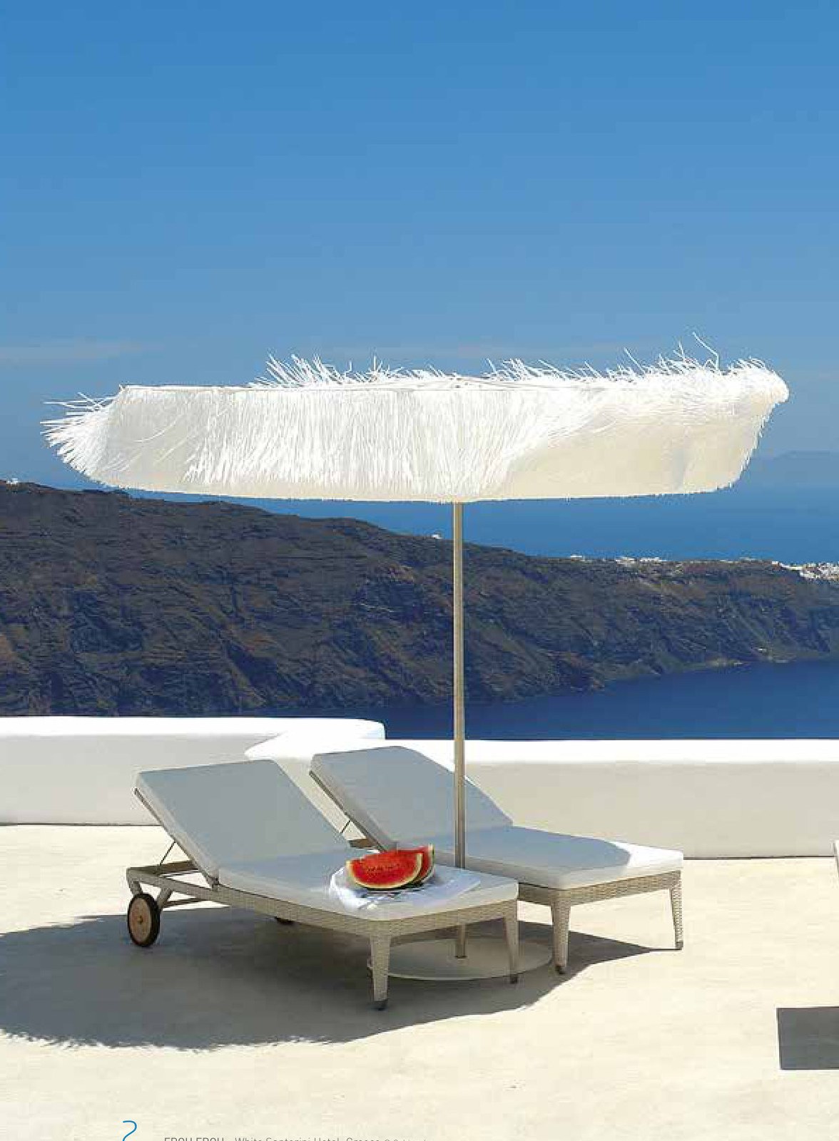 Fringed white parasol shading two sun loungers above a caldera sea view